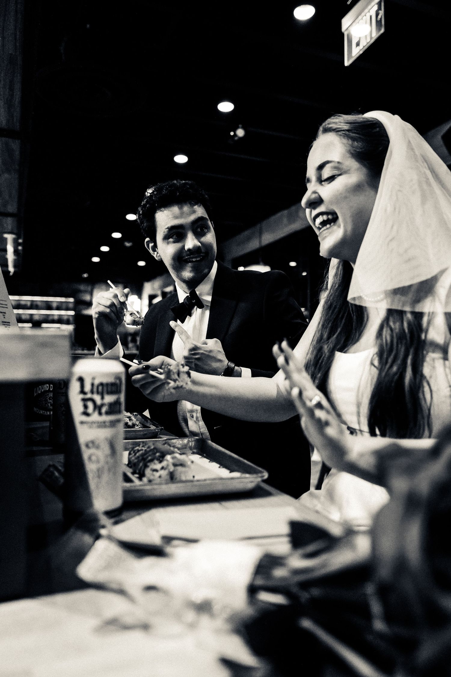 A black and white photo series showing candid moments of people conversing and laughing in a dark restaurant setting.