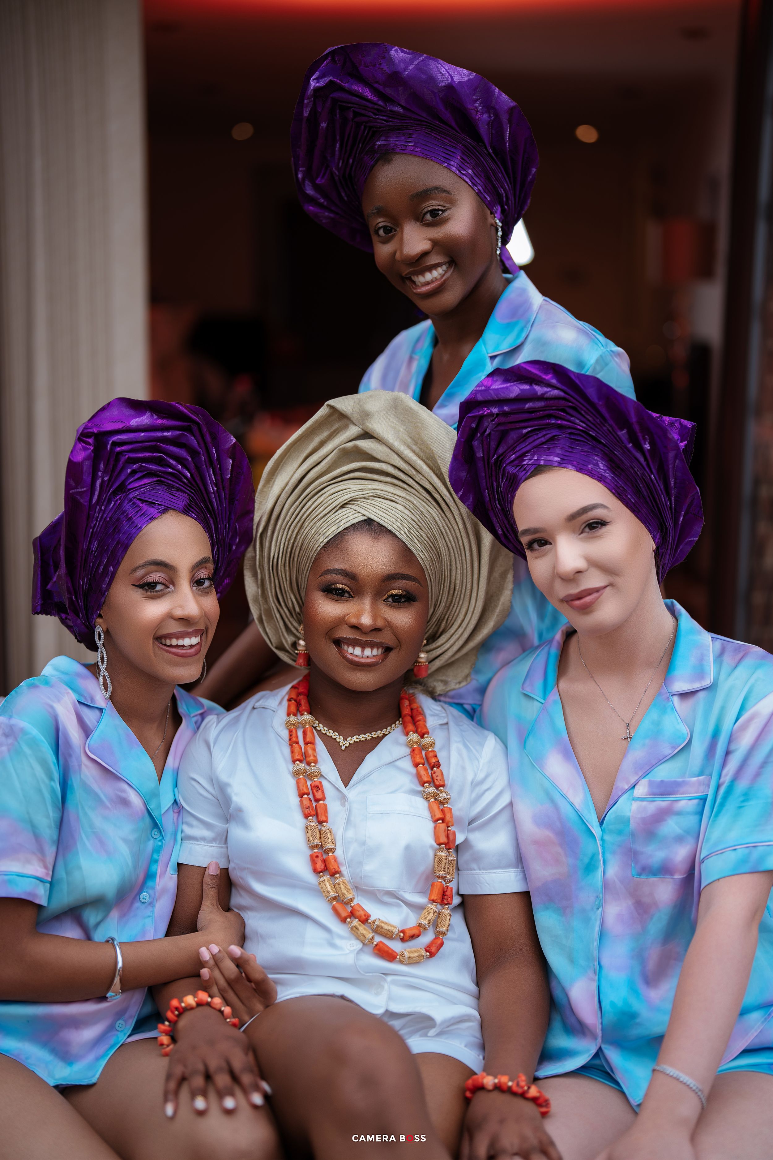 A group of women in matching light blue uniforms and vibrant purple head wraps smile together during an event.