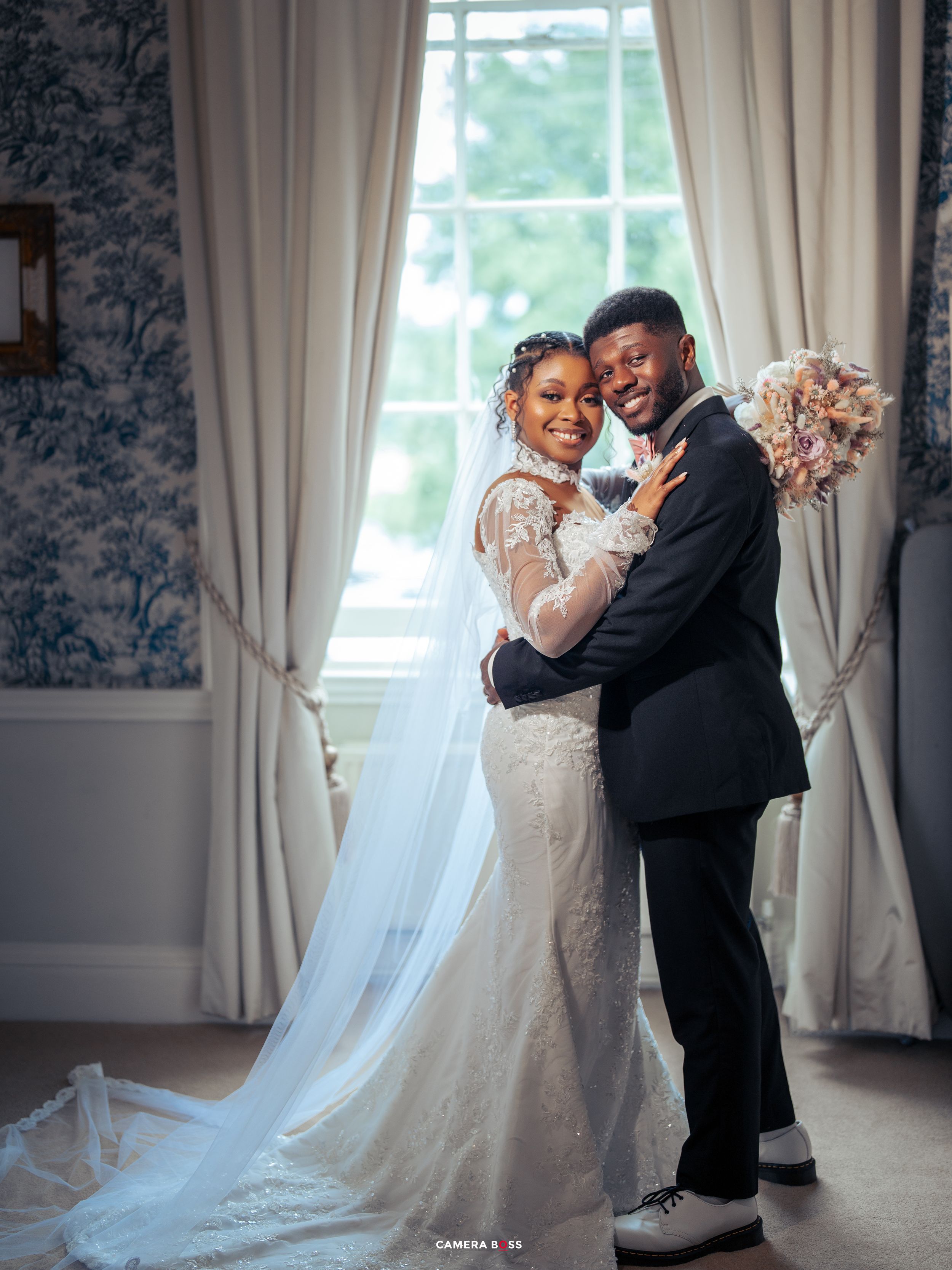 A happy couple dances together in a elegant room with white curtains and flowing bridal gown.