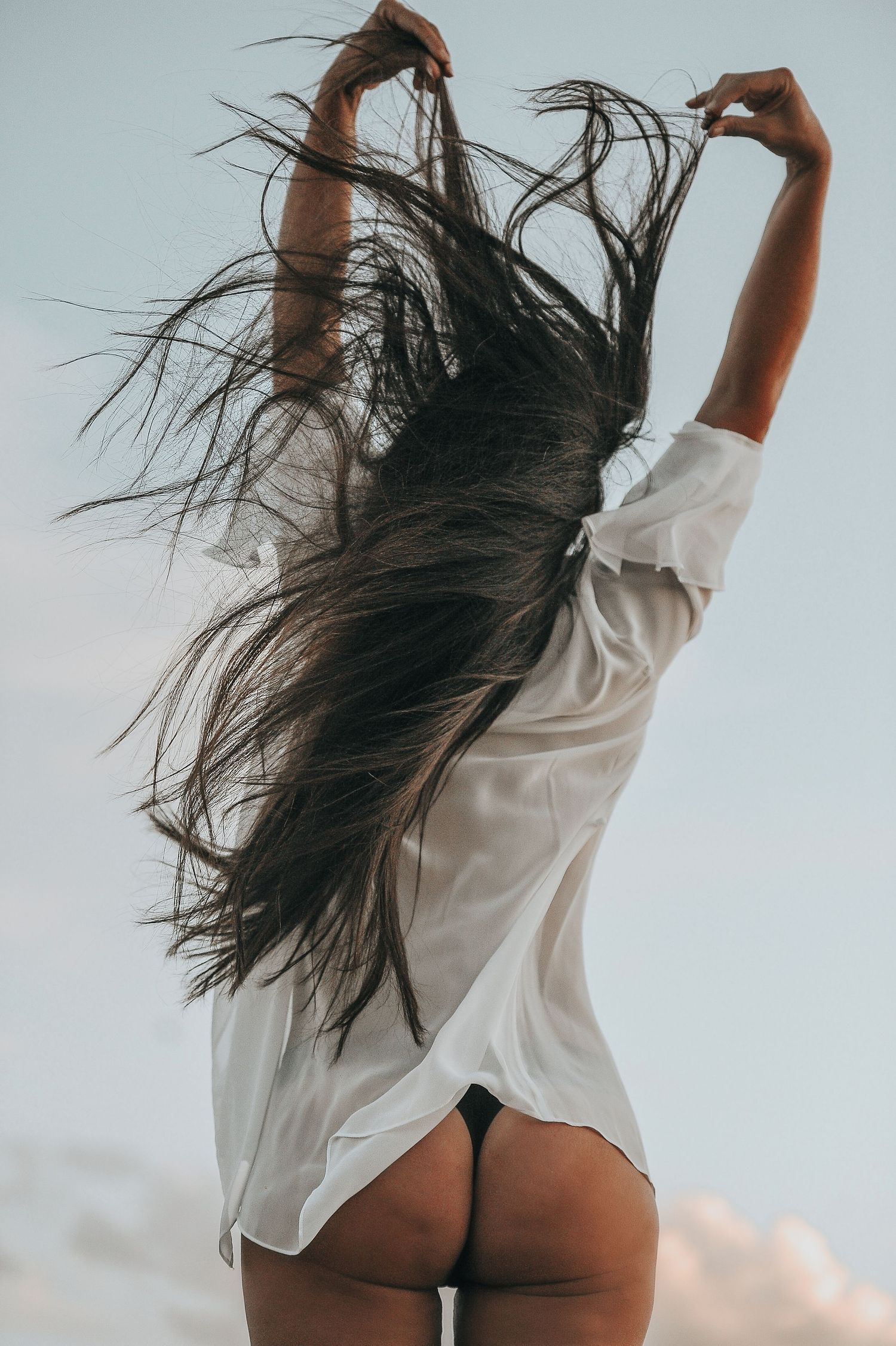 Artistic fashion series of figure in white shirt with windswept hair against blue sky.