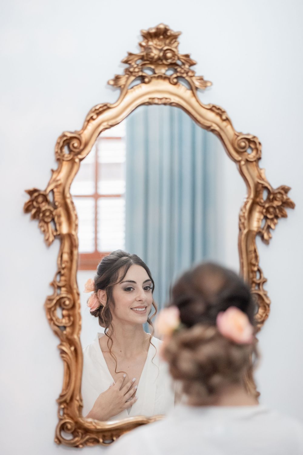 Ornate gold vintage mirror reflects delicate bridal preparations in soft light interior setting.