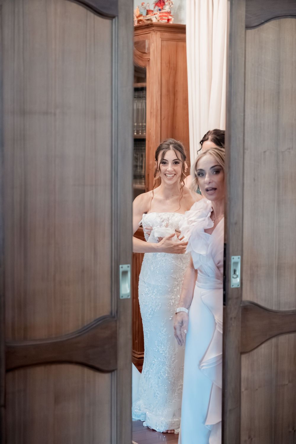 Group photo sequence showing bridal party in white dresses revealing themselves from behind a large wooden door.