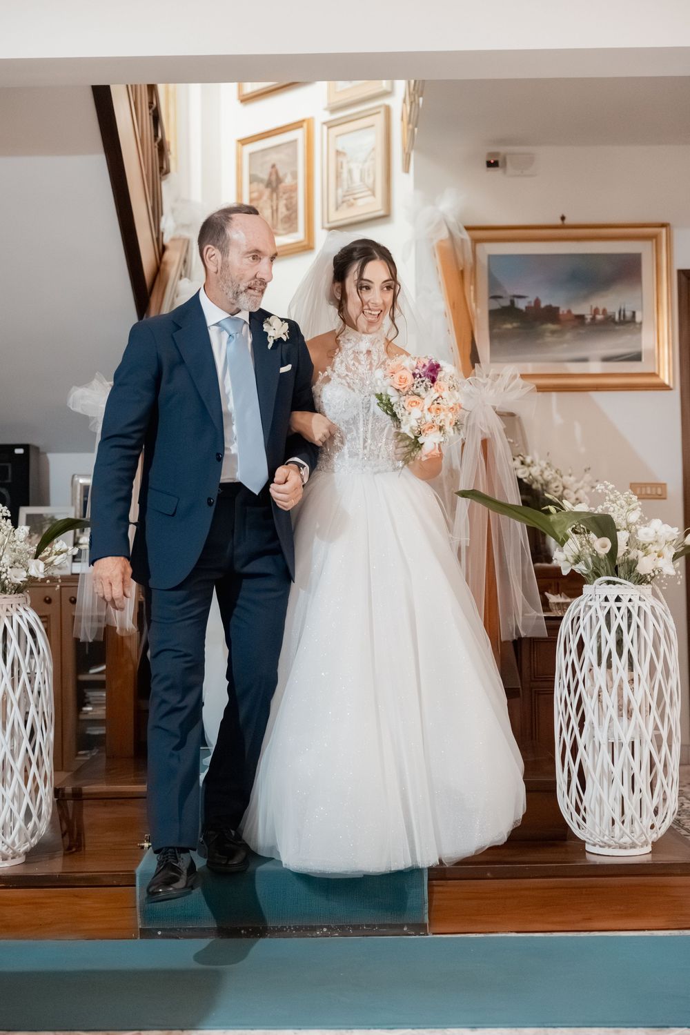 Bride and father share an emotional first look moment in a sunlit room with white lanterns and soft decor elements.