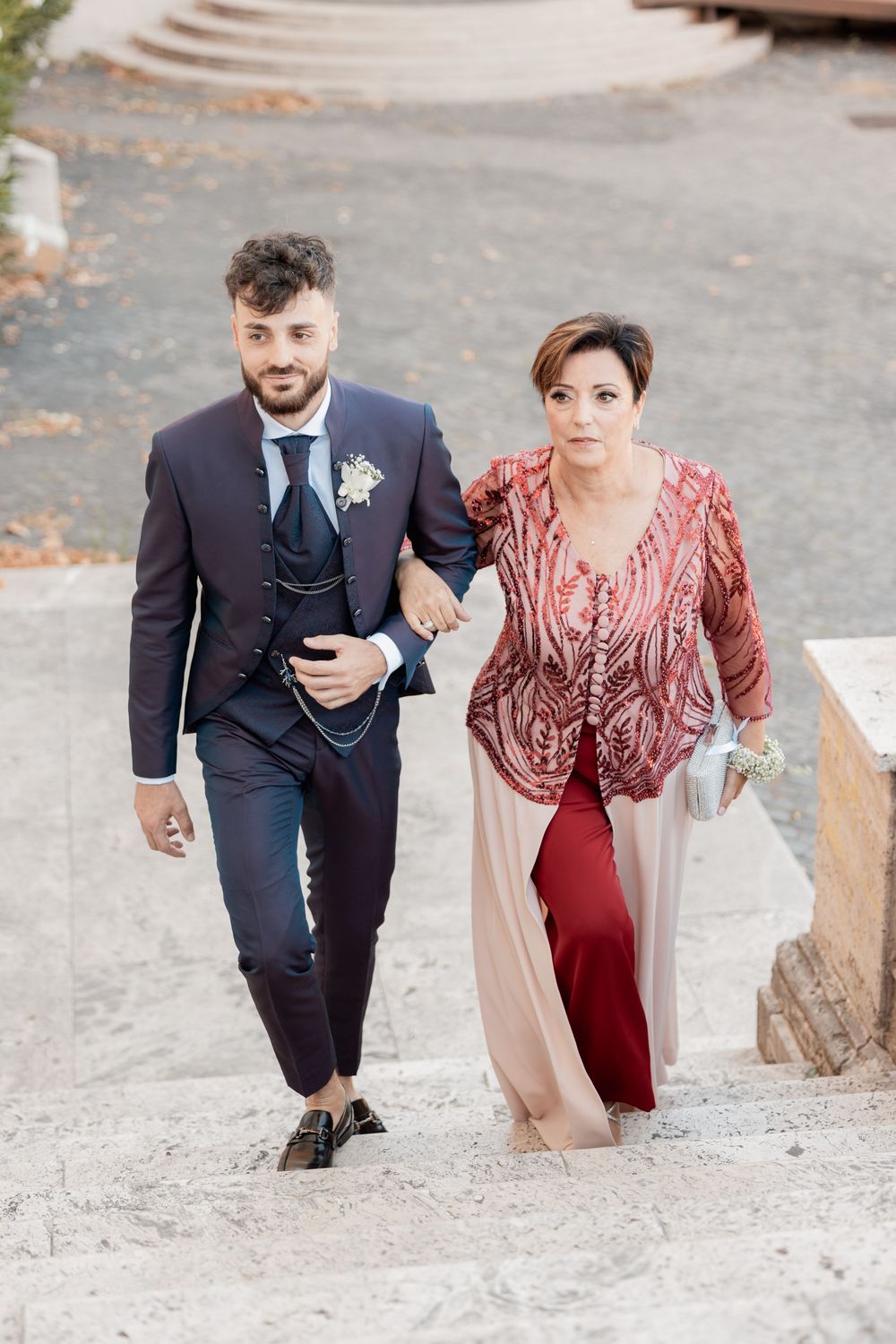 A couple in formal attire climbing up rock stairs together in an outdoor setting.