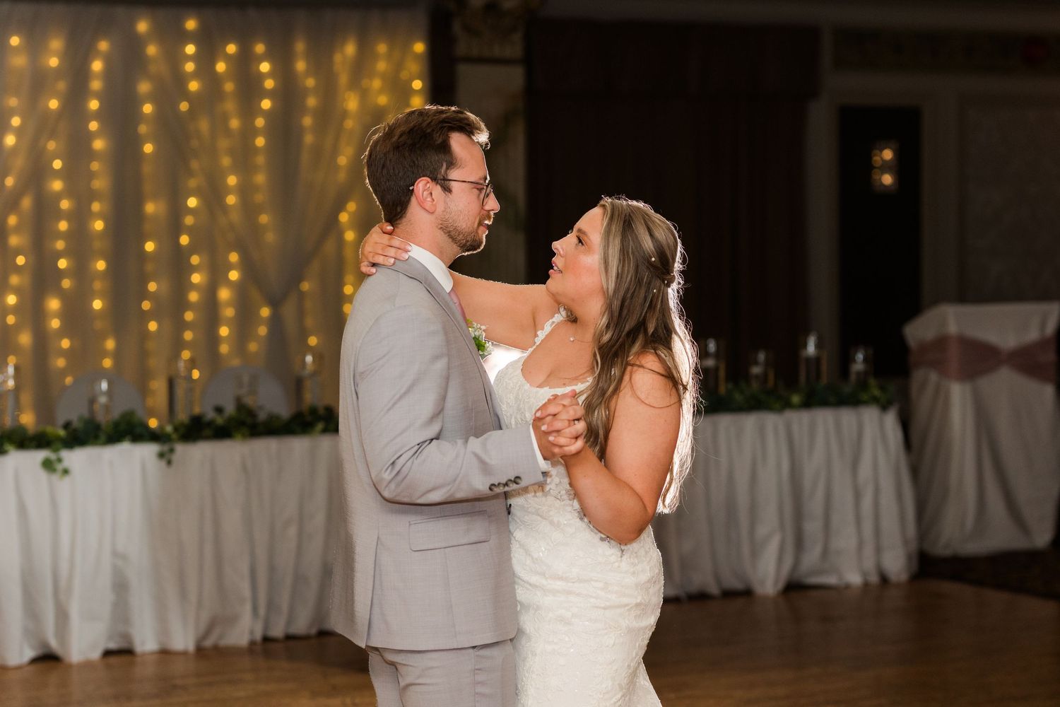 Newlyweds share a romantic first dance at their wedding reception under twinkling string lights.