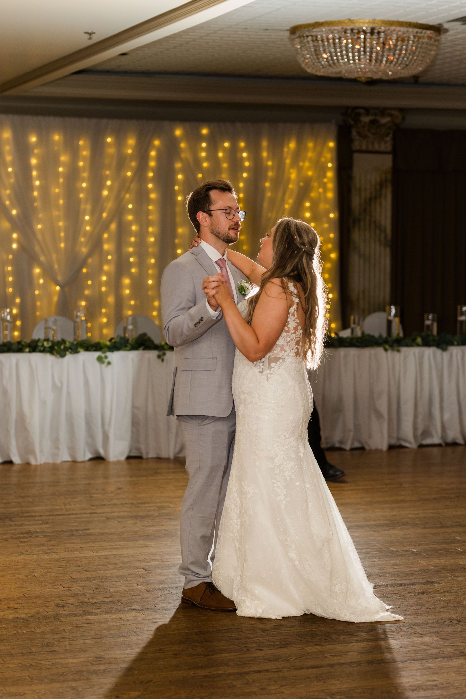 Couple sharing their first dance at a wedding reception in a ballroom decorated with twinkling lights.