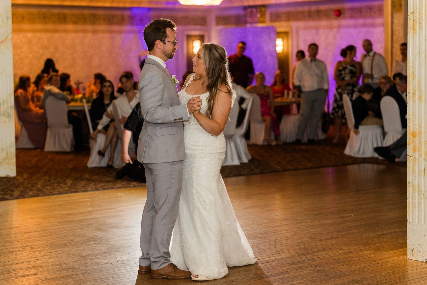 At a wedding reception, a bride and groom dance together on a glowing dance floor surrounded by guests.
