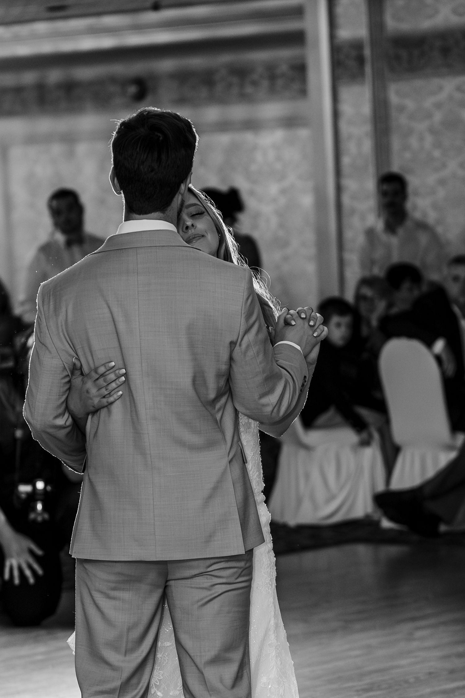 A couple shares an intimate dance together at a wedding reception, captured in black and white on a wooden dance floor.