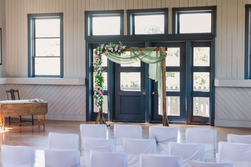 Indoor wedding ceremony setup with white chairs facing dark blue doors decorated with greenery garland and sheer fabric.