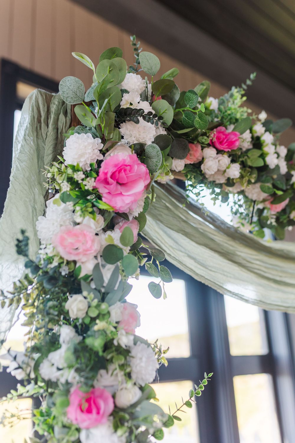 A floral wedding arch decoration featuring pink roses, white flowers and greenery draped elegantly across the top.