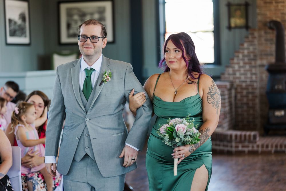 Wedding party poses in a line wearing grey suits and green accents at a brick venue.