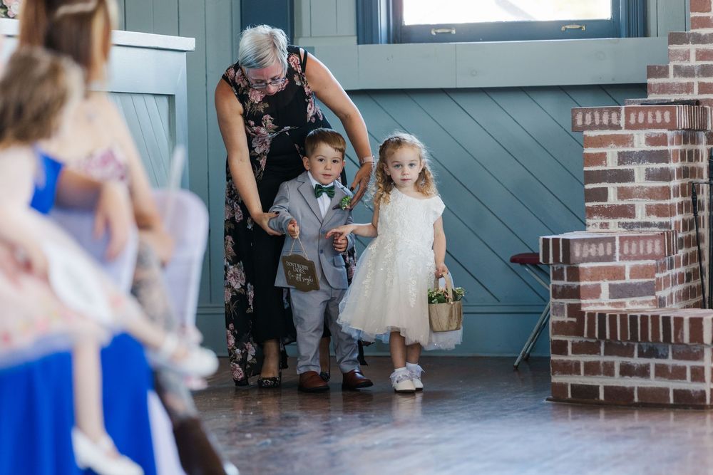 Small children dancing together at a reception in a blue-toned rustic venue with brick walls and wooden floors.