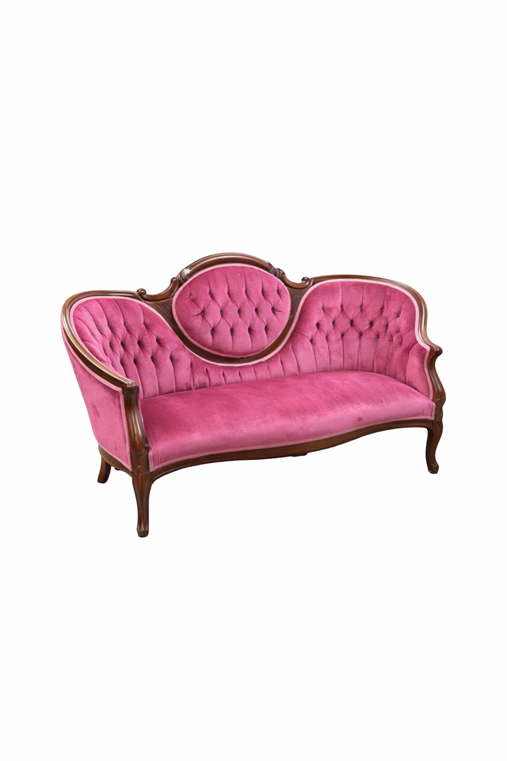 A vintage pink tufted Victorian loveseat with carved wooden frame sits on grass against bamboo plants.