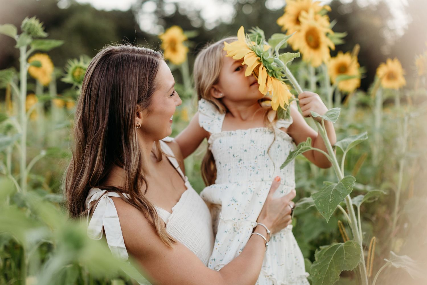 Mother and daughter sharing tender moments among sunflowers at sunset.