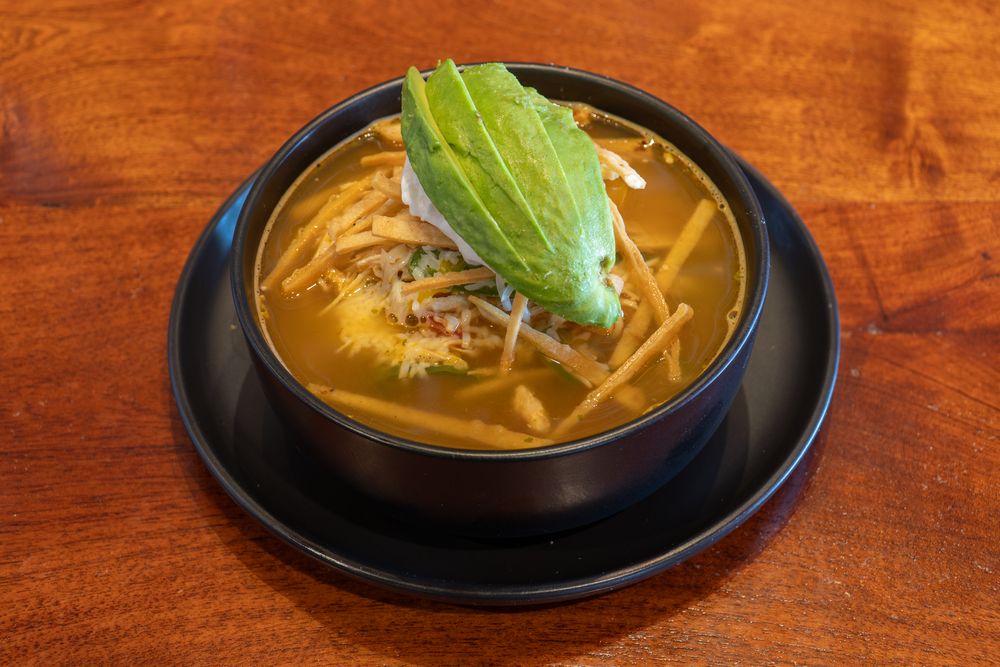 Korean-style soups and stews served in black bowls on a wooden table with vibrant garnishes.