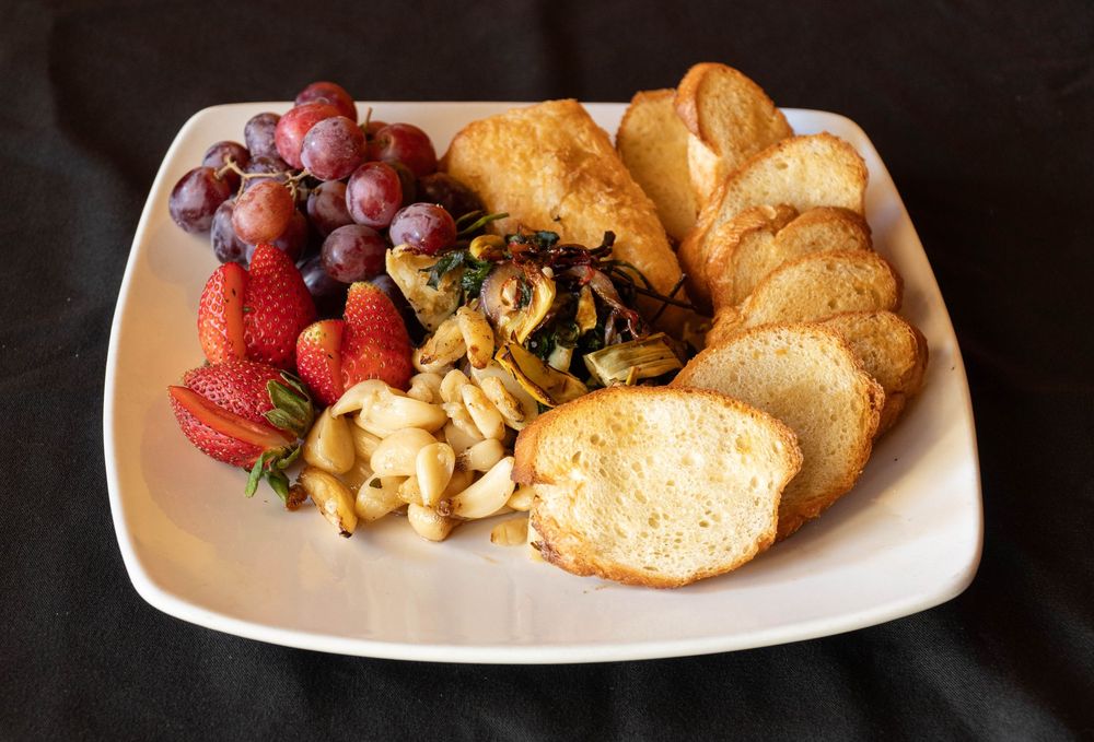 Appetizer plate with fresh fruit, toasted bread, and mixed nuts arranged on white serving dish.