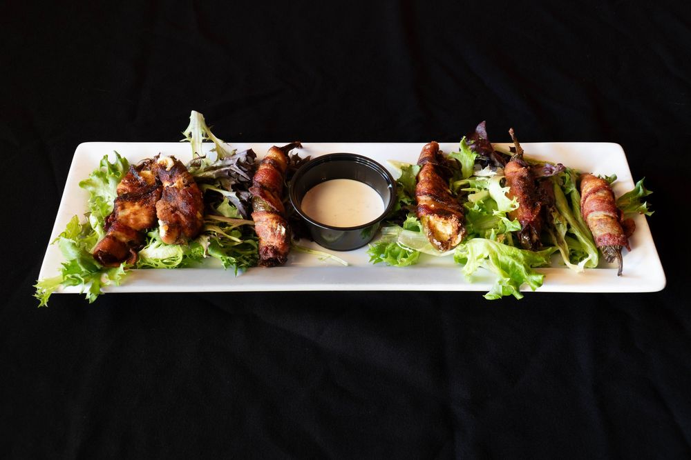 Grilled appetizers arranged on a long white platter with fresh greens and sauce.