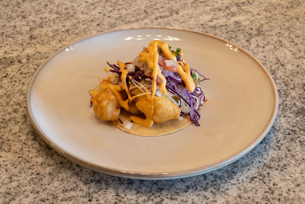Sequence of plated dishes with colorful garnishes on cream-colored plates against a stone background.