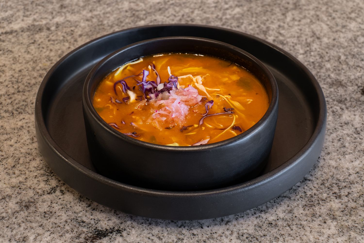Spicy orange-red soups garnished with fresh herbs served in black bowls.