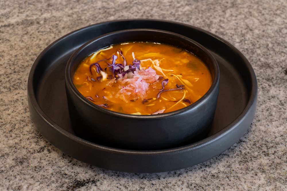 Spicy orange-red soups garnished with fresh herbs served in black bowls.