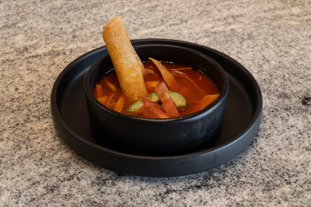 Hot soups with vegetables and meat served in black bowls on a textured stone surface.