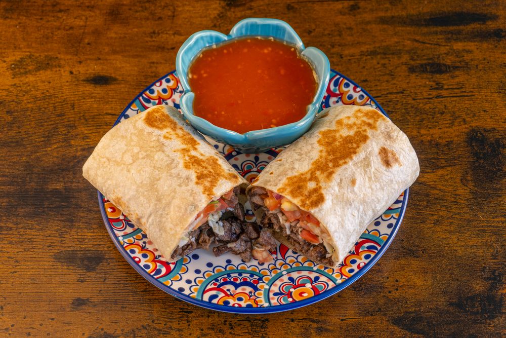 Mexican restaurant appetizer spread featuring tortilla soup and burritos on colorful patterned plates.