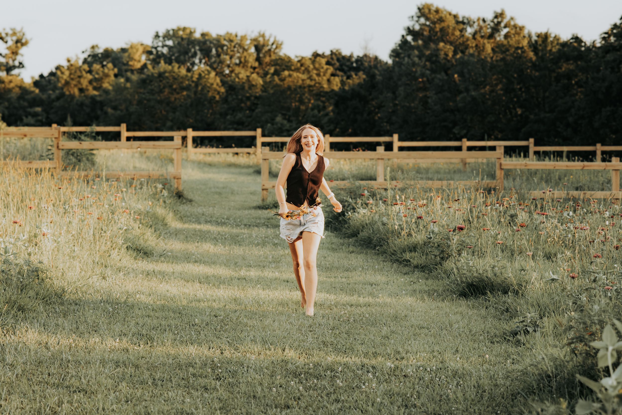 Running barefoot down a mowed path between tall grass fields at sunset.
