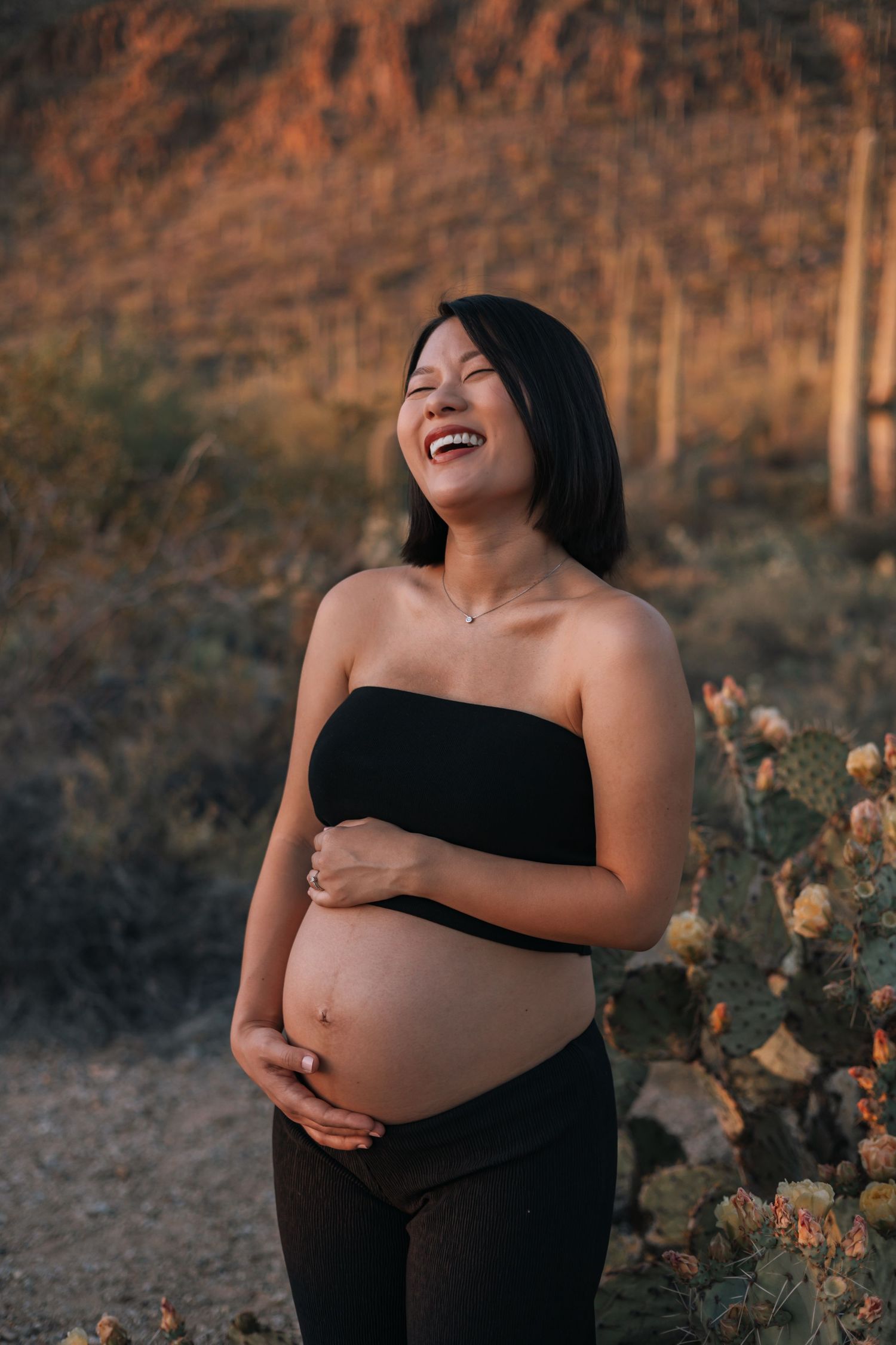 Maternity photoshoot in desert landscape with cacti at sunset.
