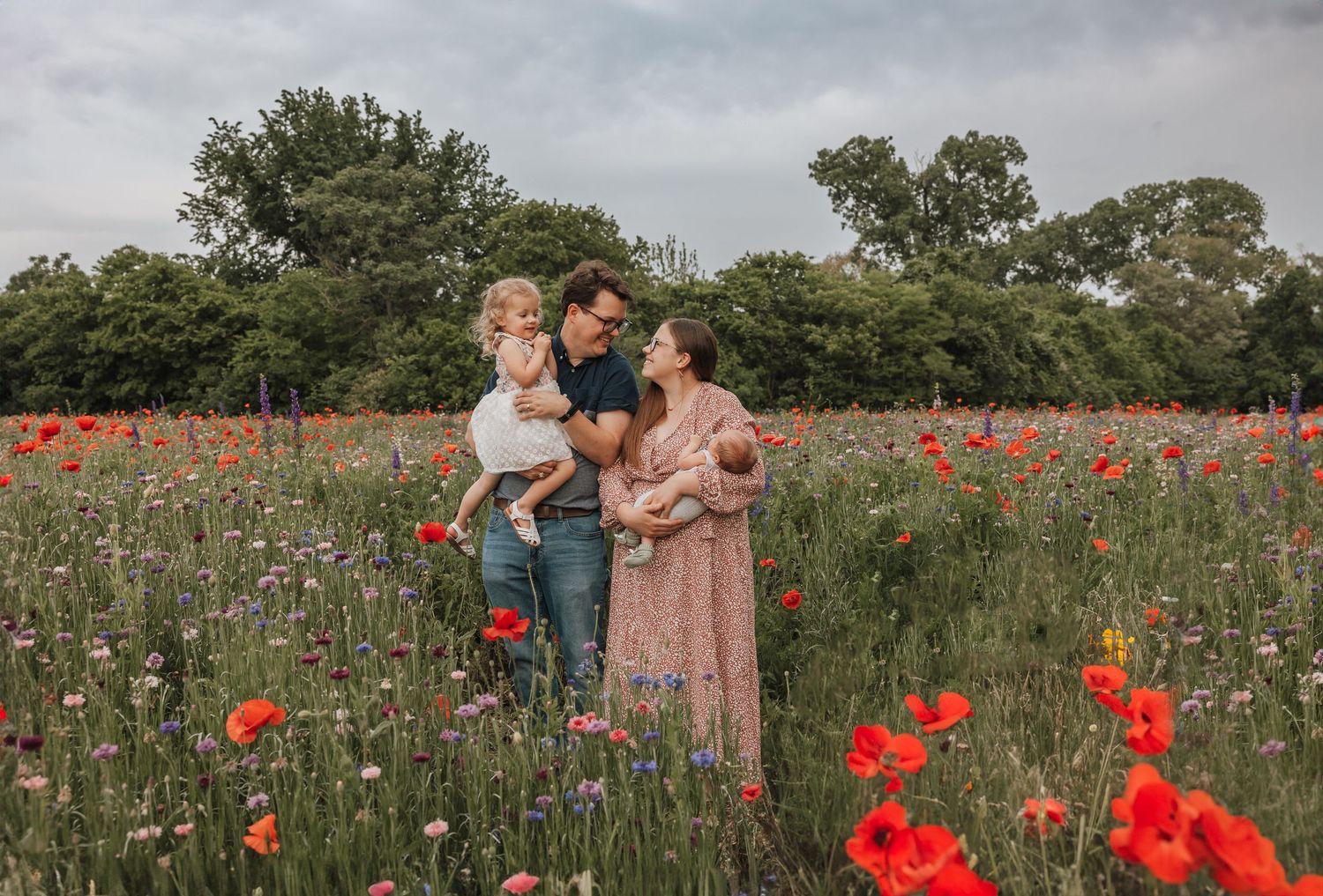 Three people stand together in a beautiful wildflower meadow filled with vibrant red poppies and purple blooms.