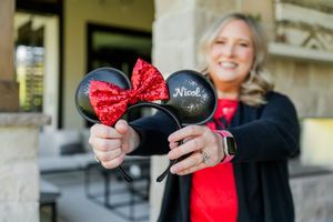 Someone holds up classic black Minnie Mouse ears with a sparkly red bow against an outdoor background.