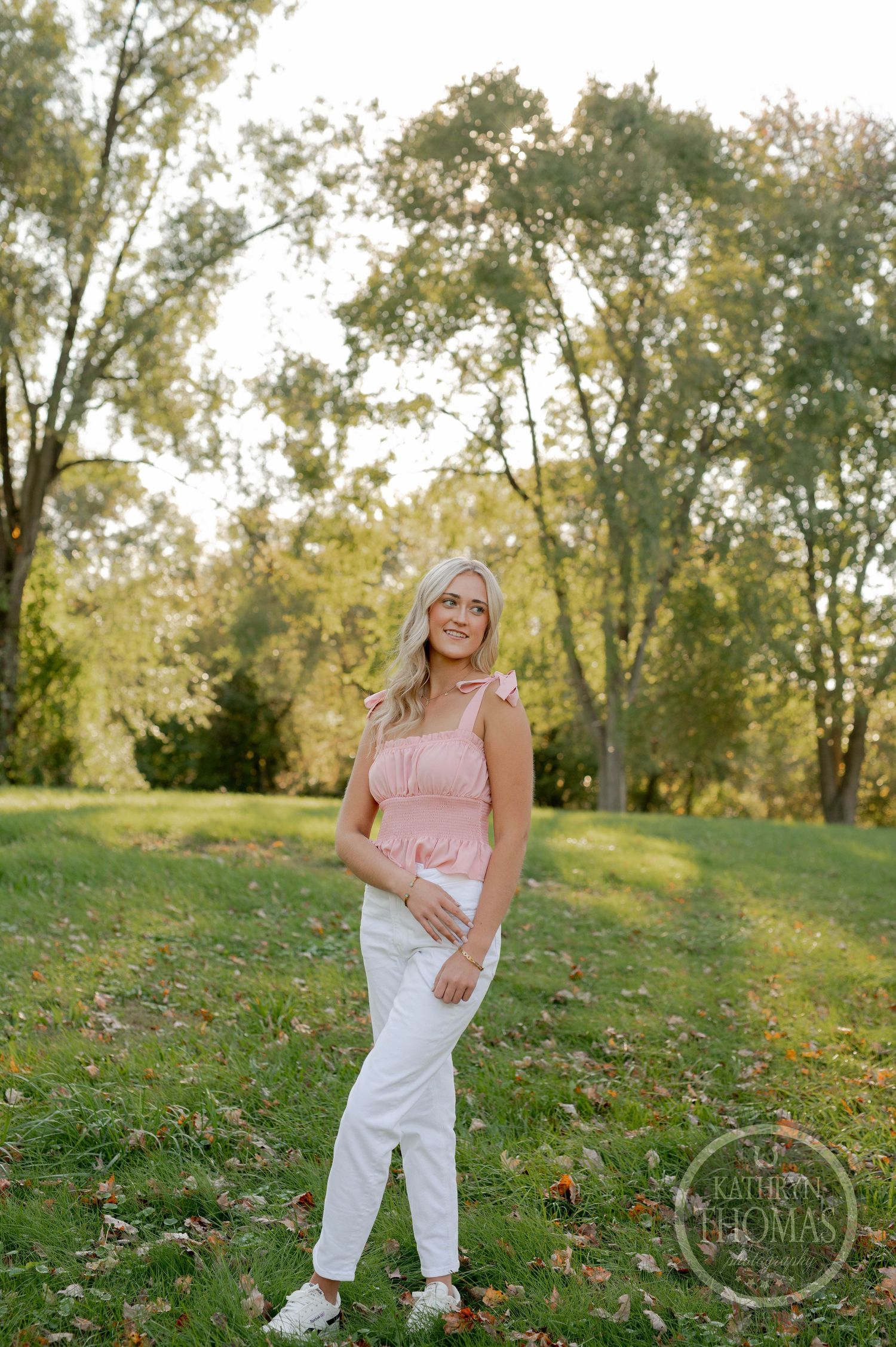 A casual outdoor photoshoot against tall trees and sunlit grass on an autumn day.