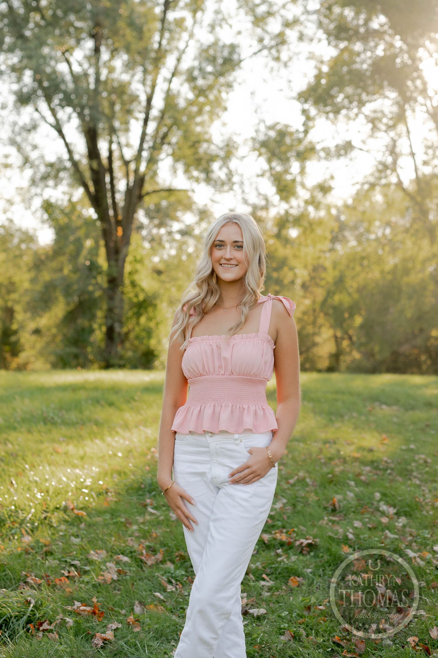 Summer fashion portrait with pink ruffle top and white pants in park setting.