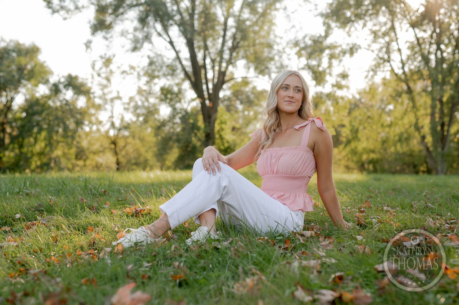 Casual outdoor photo with person in pink top relaxing on grass with autumn leaves.
