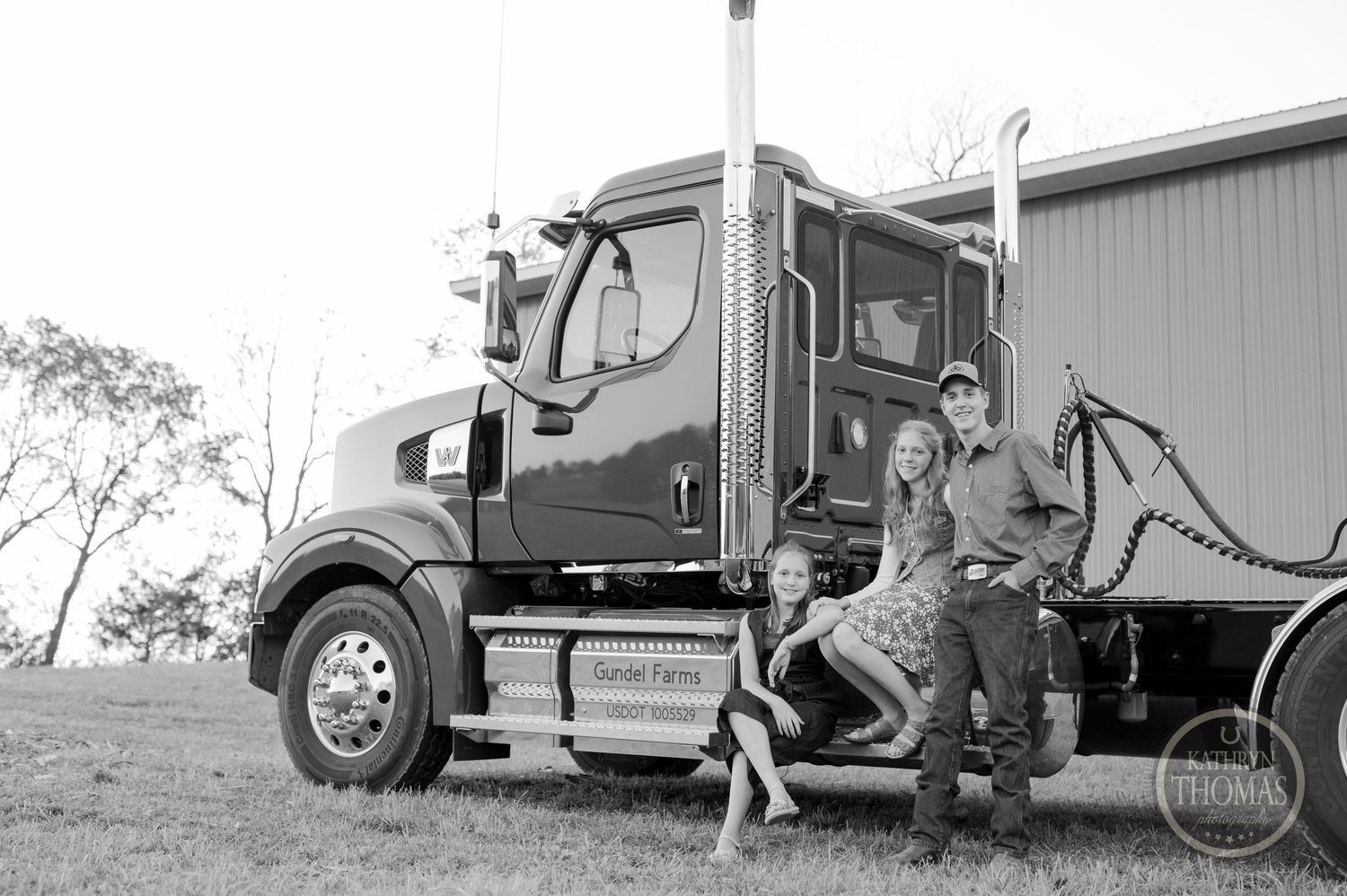 Black and white portrait of people sitting on the steps of a semi truck.