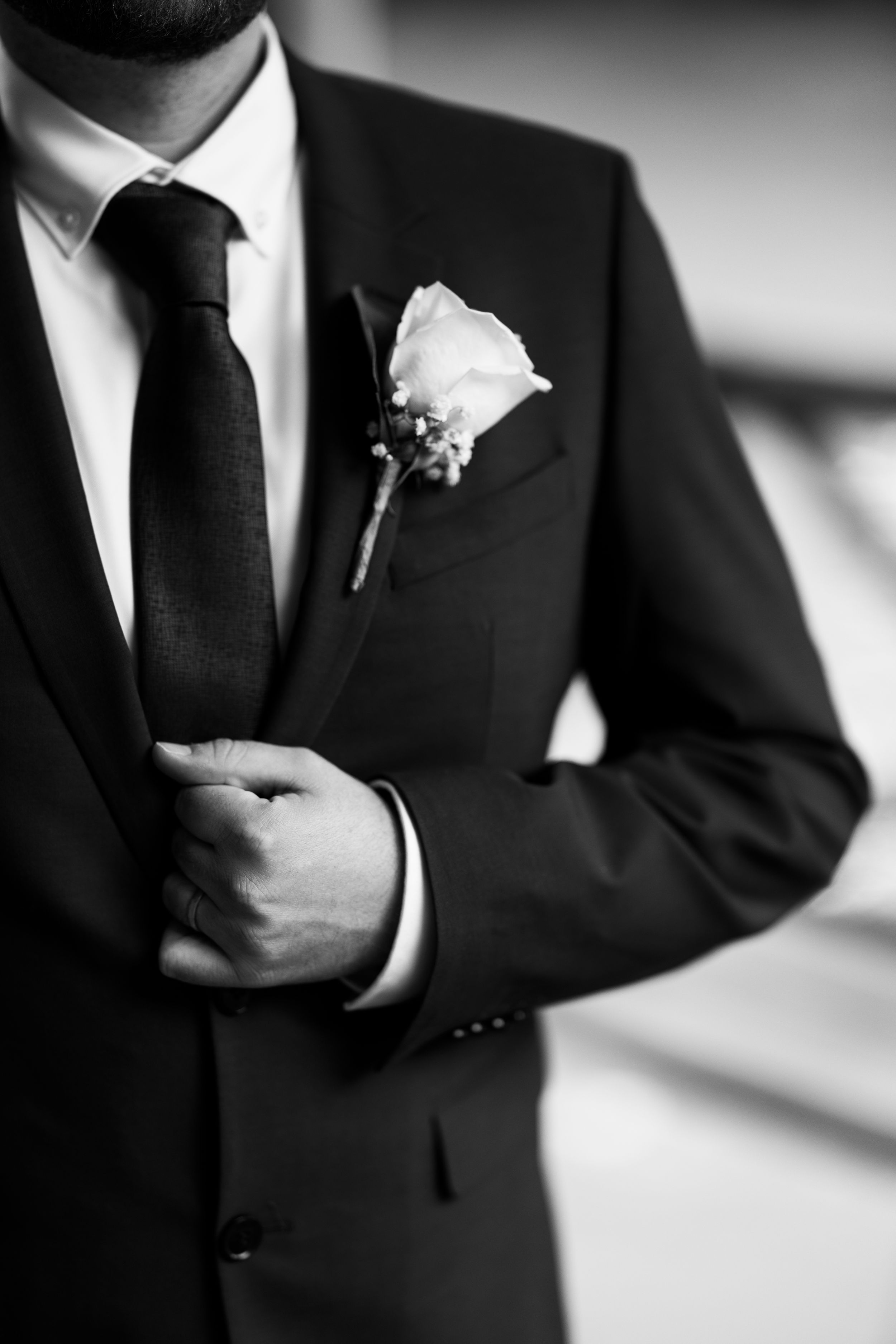A black and white detail shot of a groom's suit with a white rose boutonniere.