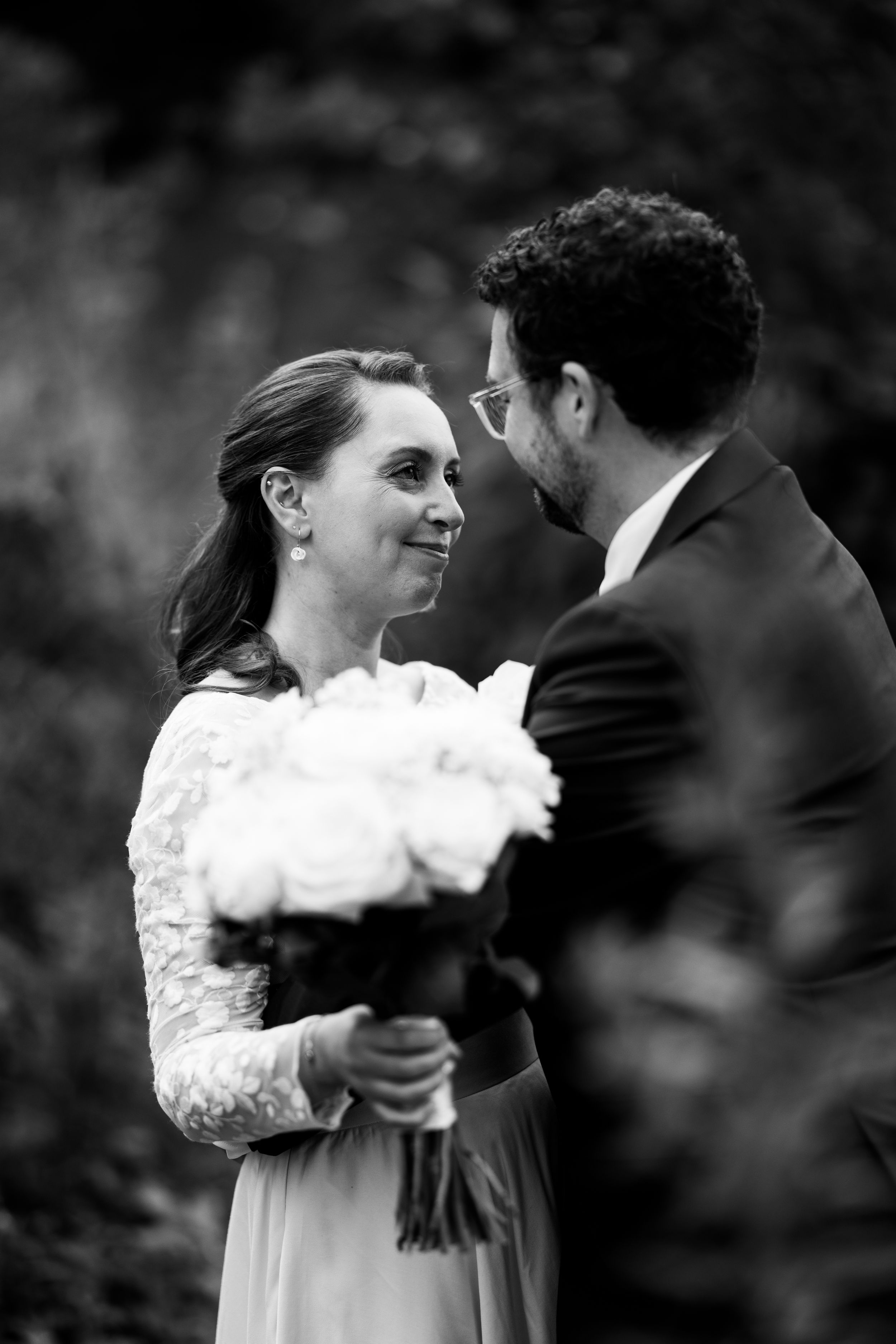 A black and white portrait of a couple sharing an intimate moment with a bouquet of white flowers.