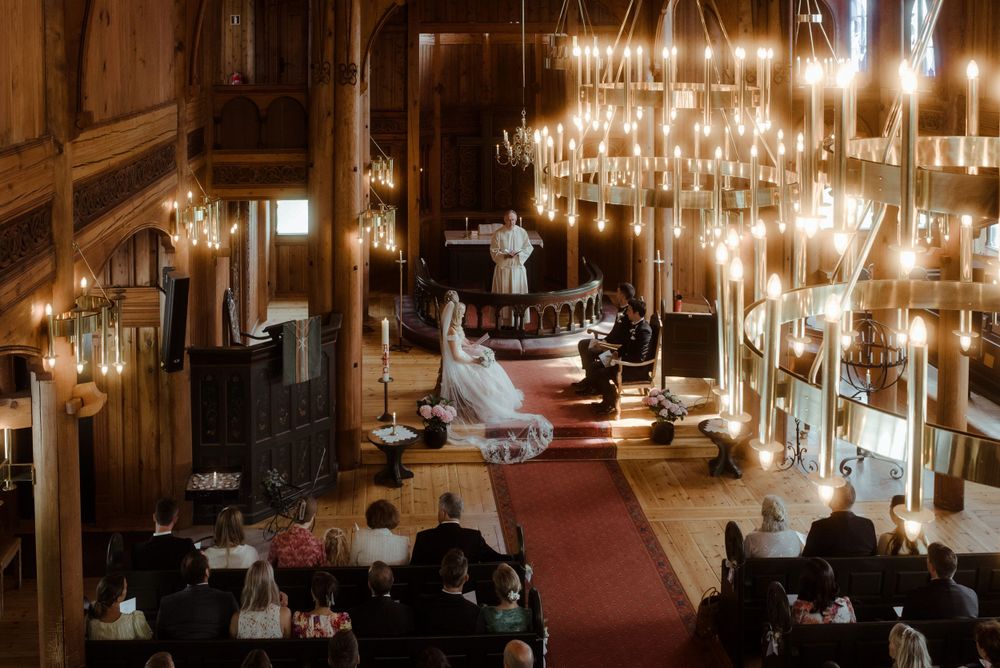 Wedding ceremony in a historic church with dramatic chandelier lighting and red carpet aisle.