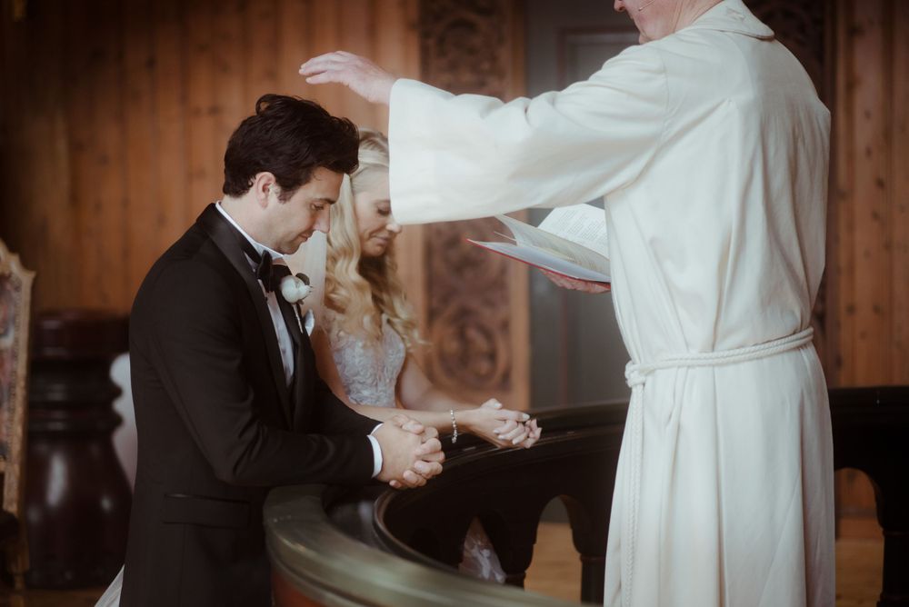 Wedding ceremony moment during a blessing in a wood-paneled church interior.