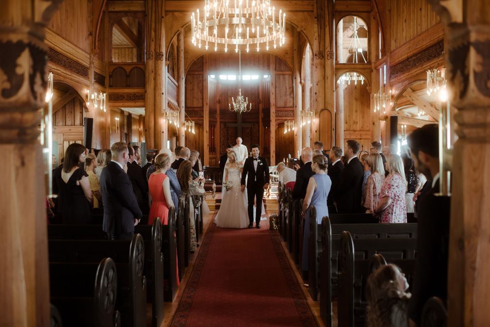 A grand church interior with chandeliers and wooden pews filled with wedding guests.