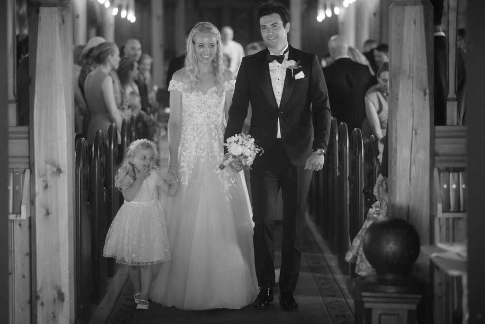 A black and white wedding photo capturing a couple walking down a church aisle.