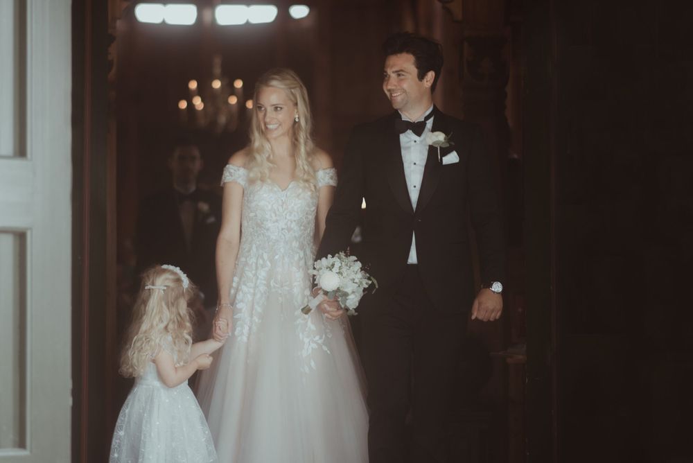 A wedding couple walks down the church aisle under warm chandelier lighting.