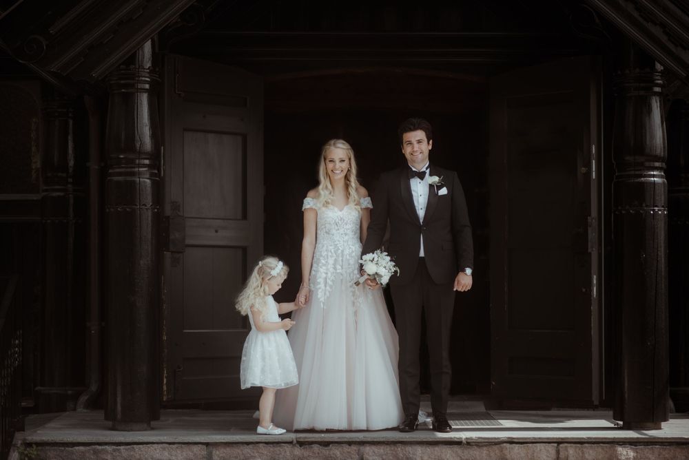 Wedding party posed in atmospheric dark wooden church entryway with flowergirl.