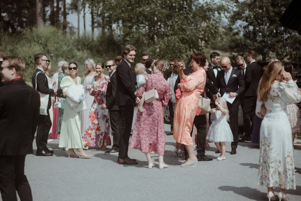 Outdoor wedding reception with guests mingling in summer dresses and formal attire.