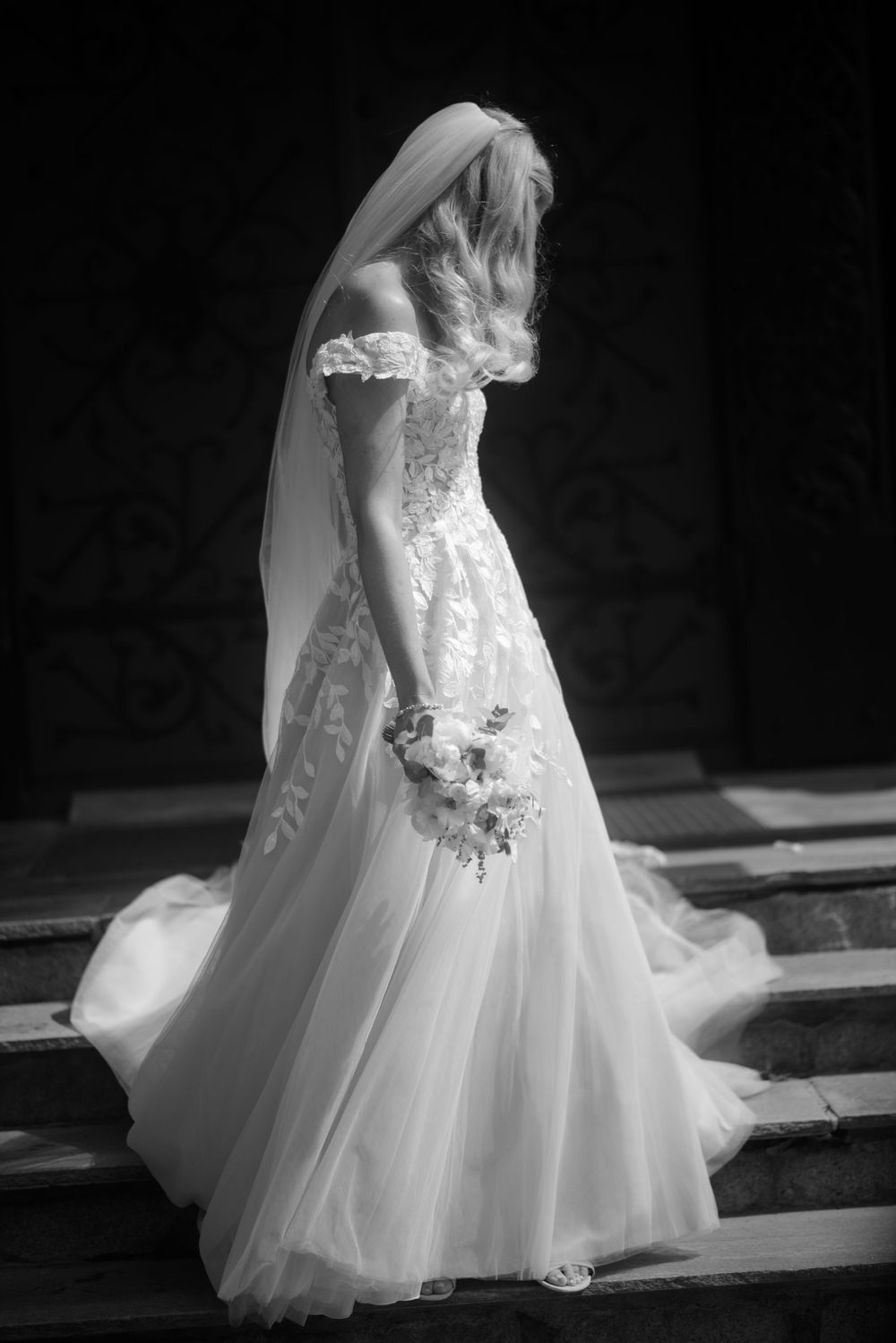 A dramatic black and white photo of a bride in a lace wedding gown on steps.