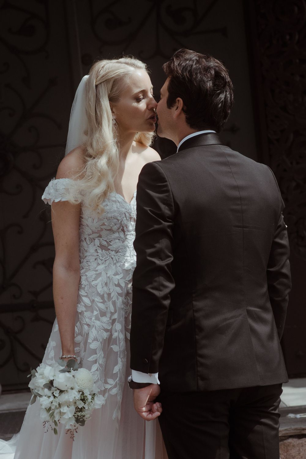 An intimate wedding kiss captured against an ornate dark background.