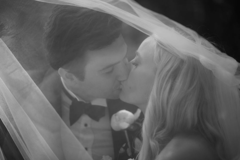 A romantic wedding moment captured under a flowing veil in black and white.