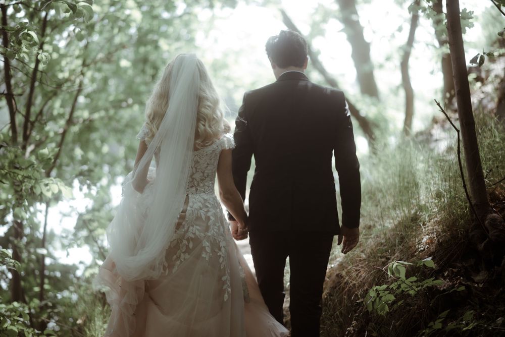 Newlyweds walking hand in hand through a misty forest path in ethereal lighting.