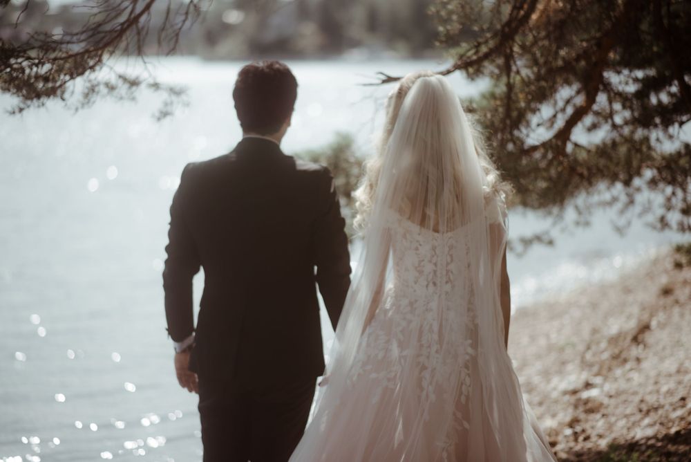 A silhouetted wedding couple stands together overlooking sparkling water.