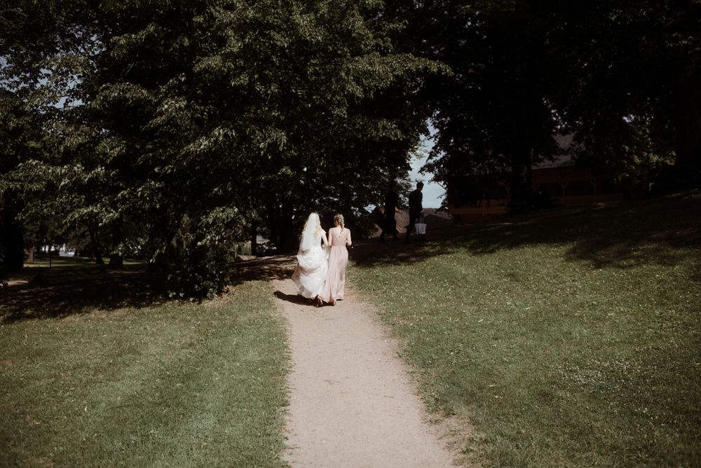 Two figures in wedding attire walking down a garden path surrounded by trees.