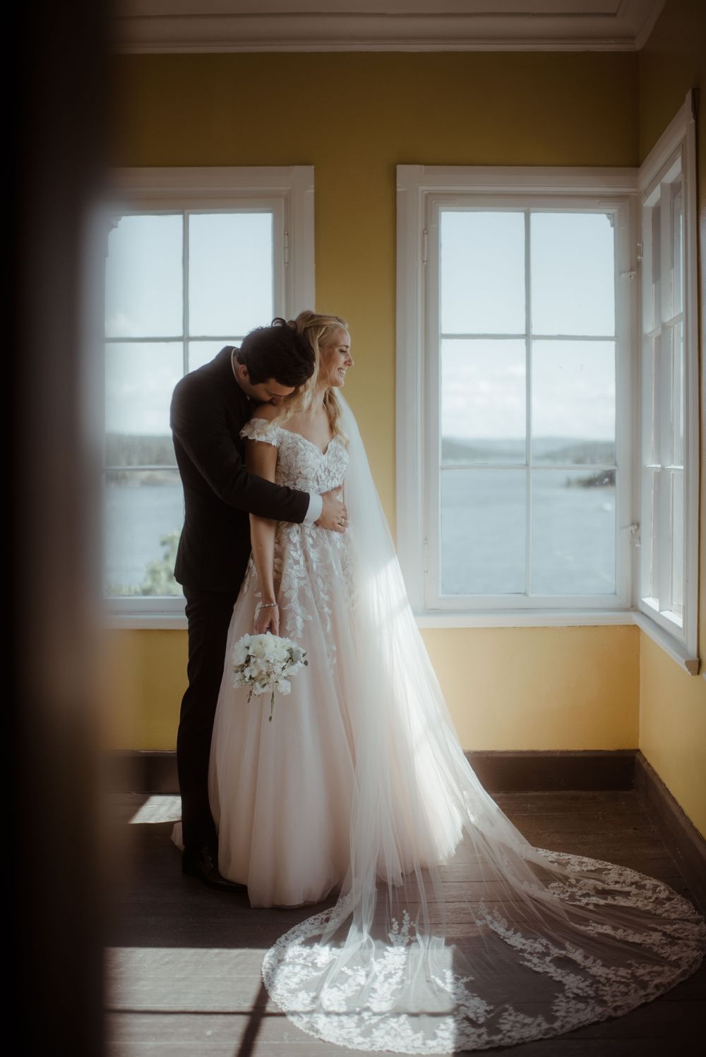 Intimate wedding moment captured in a sun-filled room with yellow walls.